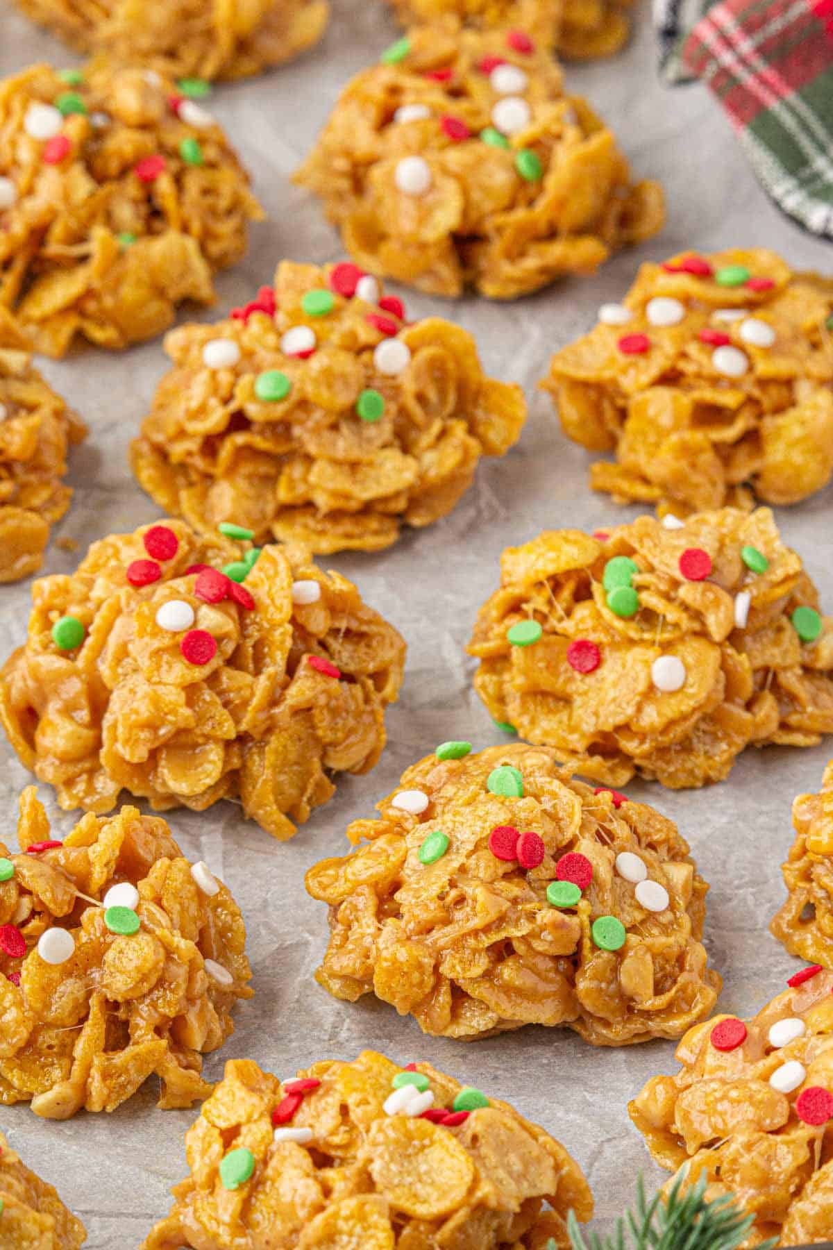 Close-up of several peanut butter cornflake cookies arranged on parchment paper, each topped with colorful holiday sprinkles and ready to serve.