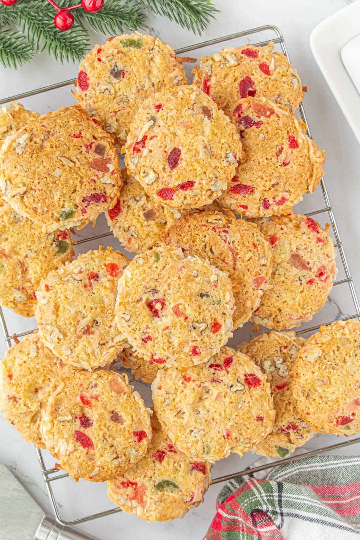 Overhead view of a cooling rack filled with cookies, golden brown with bright bits of candied fruit and toasted coconut.