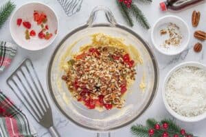 Raw cookie dough in glass mixing bowl with candied fruit and chopped pecans added.
