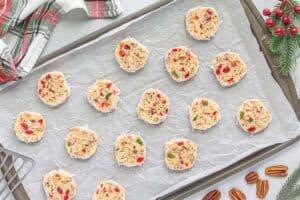 Sliced raw cookie dough rounds with coconut edges arranged on a parchment-lined baking sheet, ready to go in the oven.