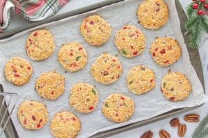 Freshly baked cookies cooling on a parchment-lined baking sheet, with golden edges and colorful cherry pieces throughout.