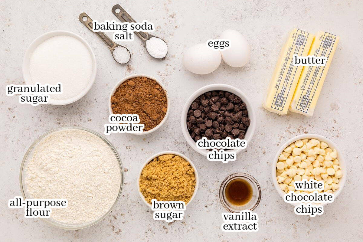 Labeled overhead image showing ingredients for triple chocolate cookies, including all-purpose flour, granulated sugar, brown sugar, cocoa powder, chocolate chips, white chocolate chips, butter, eggs, vanilla extract, baking soda, and salt.