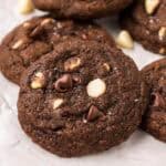 Close-up of a rich triple chocolate cookie with visible dark and white chocolate chips and a sprinkle of flaky sea salt on top.