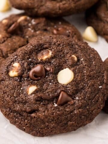 Close-up of a rich triple chocolate cookie with visible dark and white chocolate chips and a sprinkle of flaky sea salt on top.