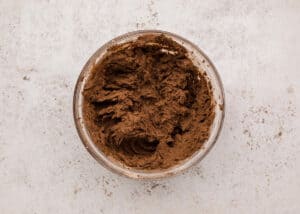 Glass bowl containing thick chocolate cookie dough after cocoa powder has been added and fully blended.