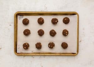 Evenly spaced scoops of chocolate cookie dough with white chocolate chips on a parchment-lined baking tray, ready for baking.
