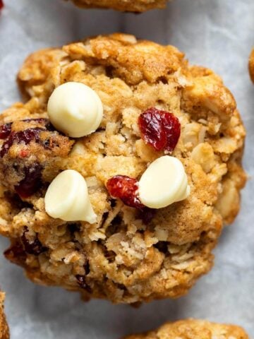 Tightly cropped image showing the texture of a single cranberry white chocolate oatmeal cookie, highlighting the chewy oats and studded mix-ins.
