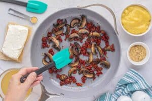 Sundried tomatoes and mushrooms sauteed in a skillet. Cream cheese, seasoning, cream soup and chicken stock surround the pan.