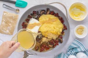 Sauteed sun-dried tomatoes and mushrooms in a skillet. Cream of chicken soup, cream cheese and chicken stock is being poured into the skillet.