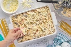 Cheese being sprinkles over the top of a casserole dish before baking.