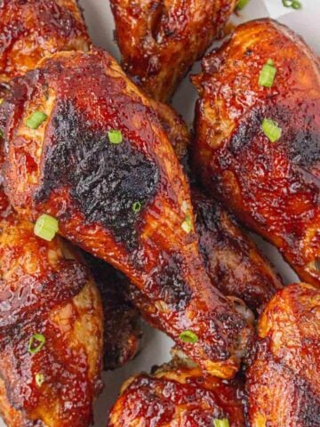 Platter of baked BBQ chicken drumsticks piled together, glistening with sauce and sprinkled with green onions.