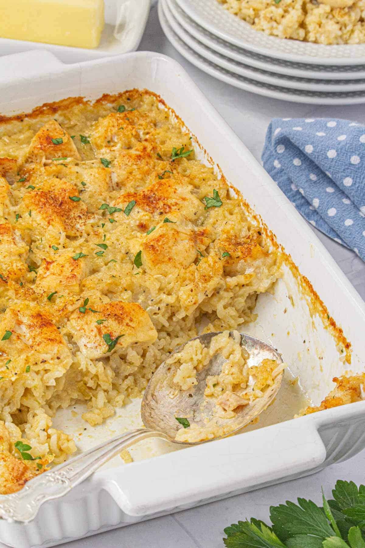 White casserole dish with a serving of creamy chicken and rice removed, showing the rich texture and golden topping.