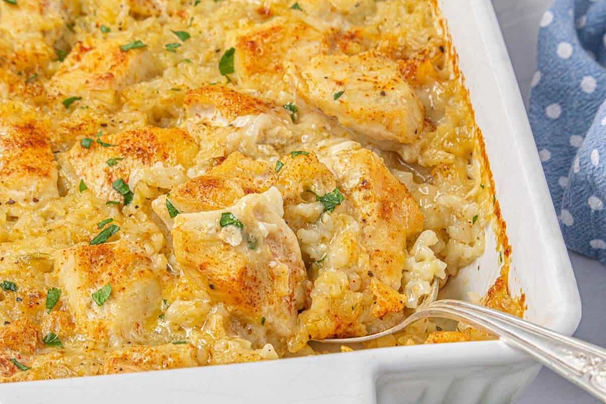 Golden-brown baked chicken casserole being served from the baking dish with a silver spoon.