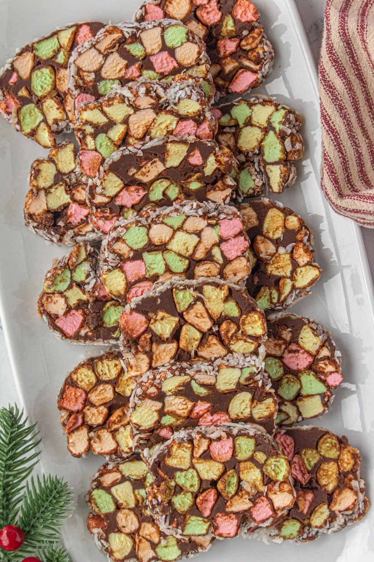 A white platter filled with slices of church window candy, surrounded by festive holiday decor.