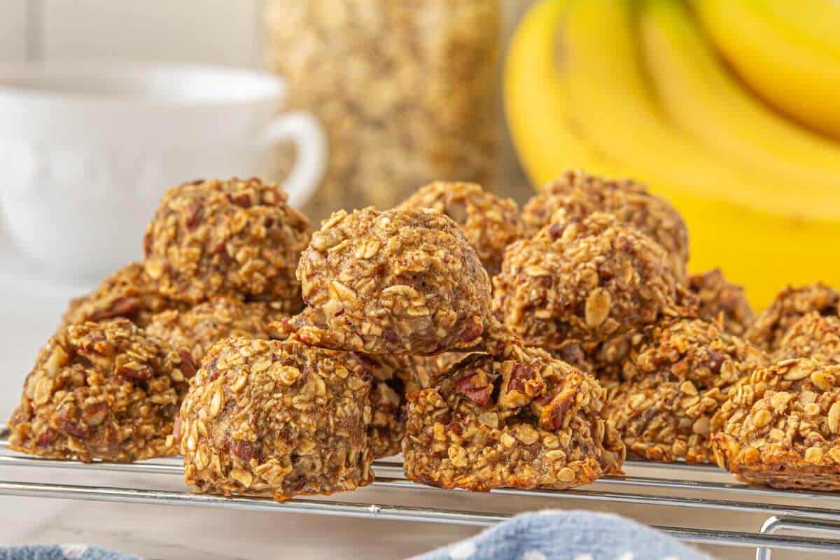 Oatmeal cookies on a cooling rack with a bunch of bananas in the background.