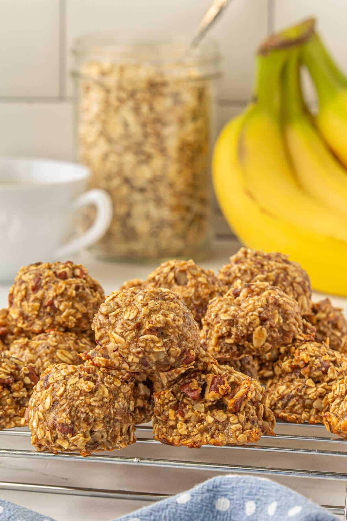 Instant Oatmeal cookies on a cooling rack. In the background is bunch of bananas, a coffee cup and oatmeal in a clear glass container.