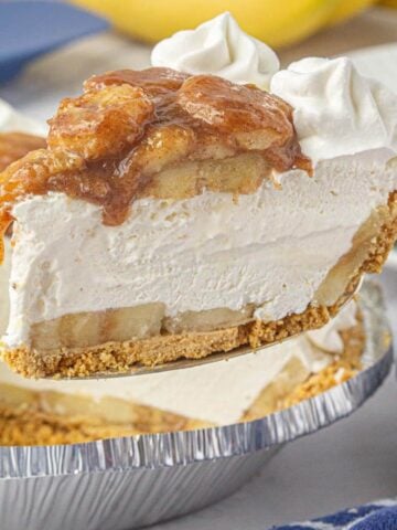 A whole no-bake bananas foster pie with a slice being lifted out, showing the creamy layers, banana filling, and caramelized topping.