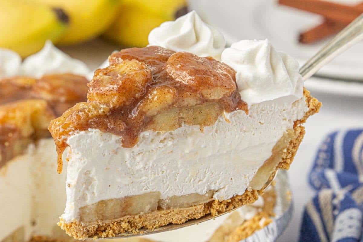 A slice of no-bake bananas foster pie on a plate with a fork, showing layers of bananas, fluffy cream filling, and graham cracker crust.