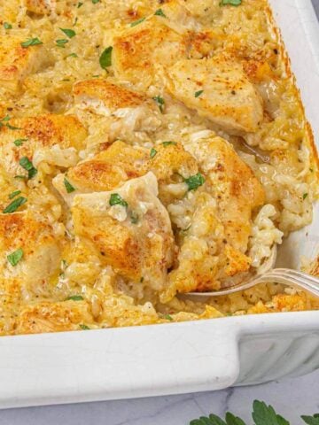 White casserole dish with a serving of creamy chicken and rice removed, showing the rich texture and golden topping