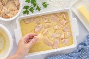 Uncooked chicken pieces being placed over a creamy rice mixture in a white casserole dish, ready for baking.