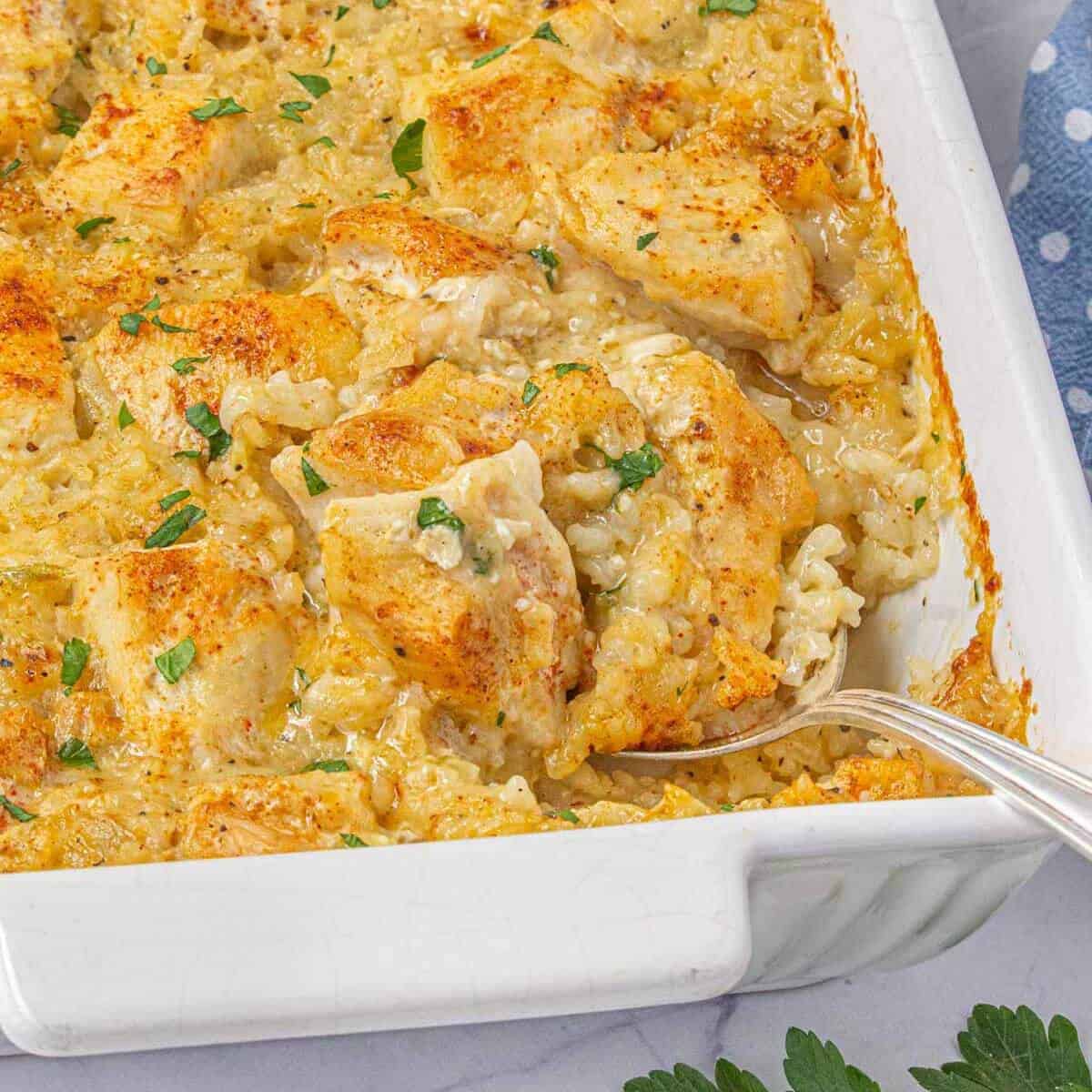 White casserole dish with a serving of creamy chicken and rice removed, showing the rich texture and golden topping