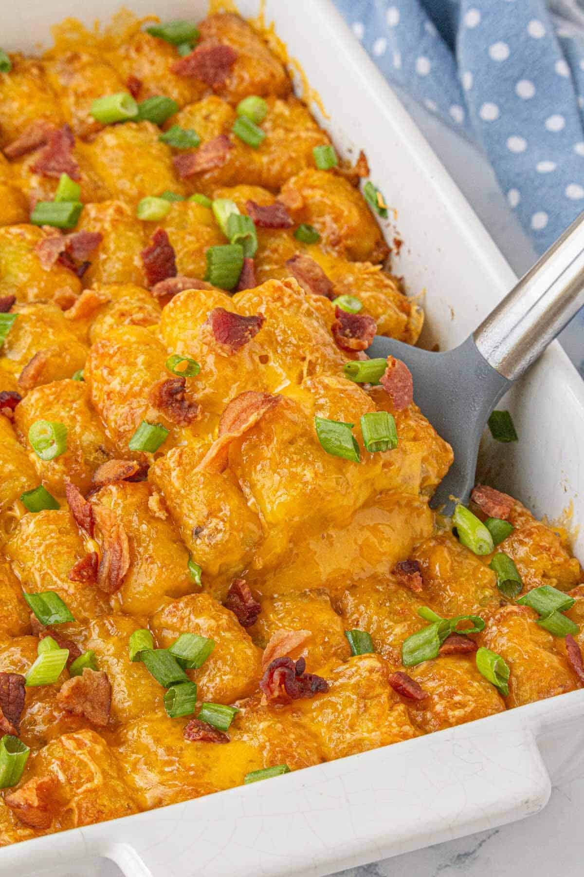 Fully baked bacon cheeseburger tater tot casserole topped with melted cheddar, crispy bacon, and chopped green onions.