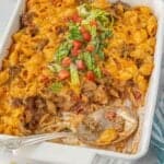 Baked cheeseburger pasta casserole in a white dish, topped with shredded lettuce and tomatoes, with a large serving spoon in the corner.