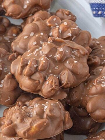 Close-up of chocolate peanut clusters on a white plate, topped with flakes of sea salt.