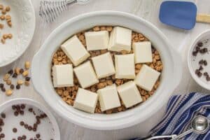 Crockpot filled with peanuts and peanut butter chips, topped with large chunks of white almond bark before melting.