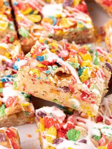 Close-up of Fruity Pebbles blondies cut into squares, topped with colorful cereal and drizzled with white glaze.