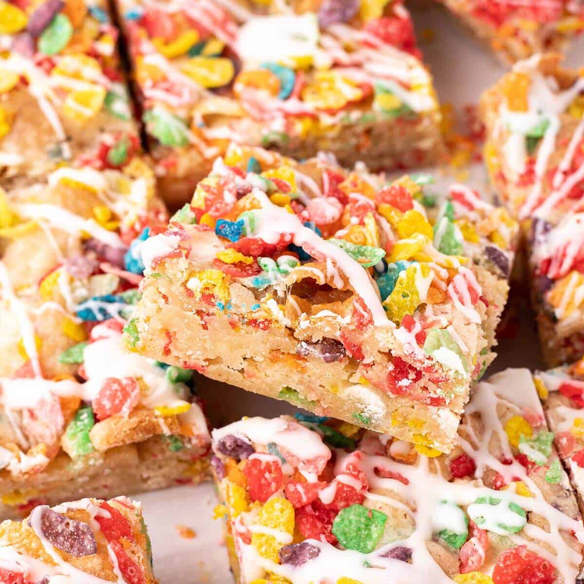 Close-up of Fruity Pebbles blondies cut into squares, topped with colorful cereal and drizzled with white glaze.