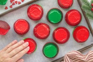 Cupcakes flipped upside down onto parchment-lined baking sheet, one being gently pressed by hand.