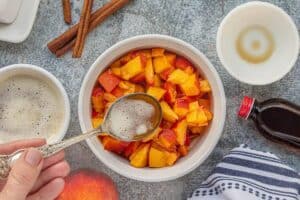 Fresh diced peaches in a bowl being drizzled with browned butter for extra flavor.