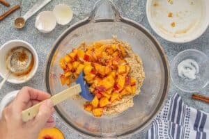 Fresh peaches being folded into the quick bread batter with a spatula in a mixing bowl.