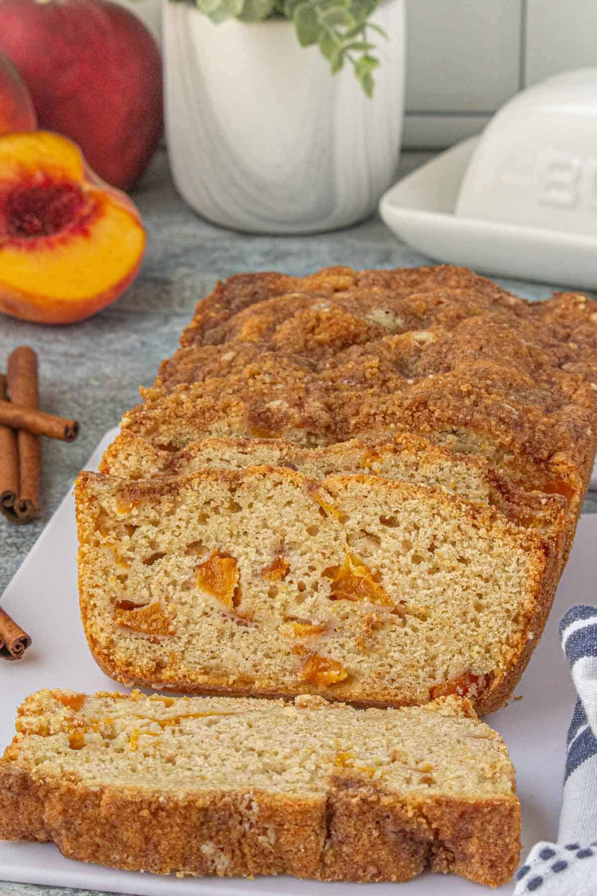 Freshly baked peach quick bread on a cutting board, showing its crisp crumble topping and soft, moist interior..