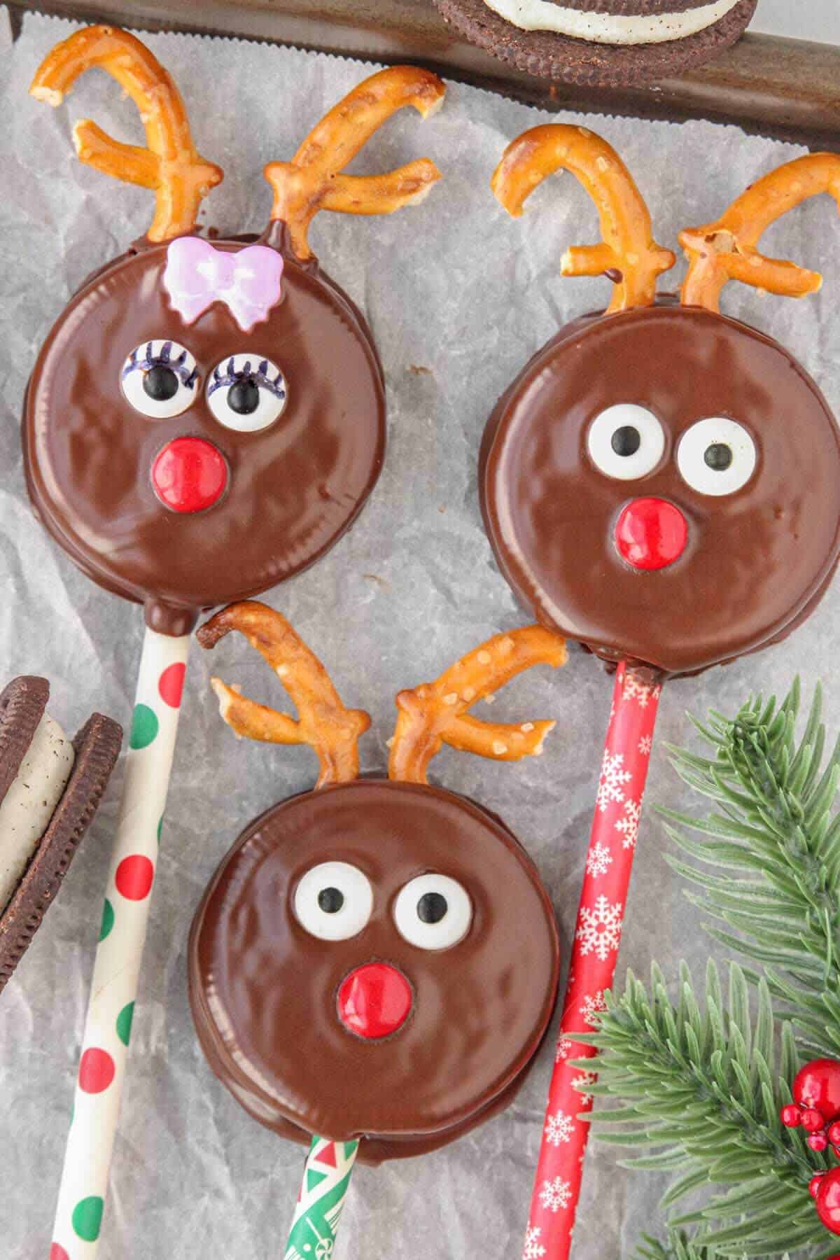 An overheat photo of 3 Oreo Reindeer Pops displayed on parchment paper with holiday greenery.