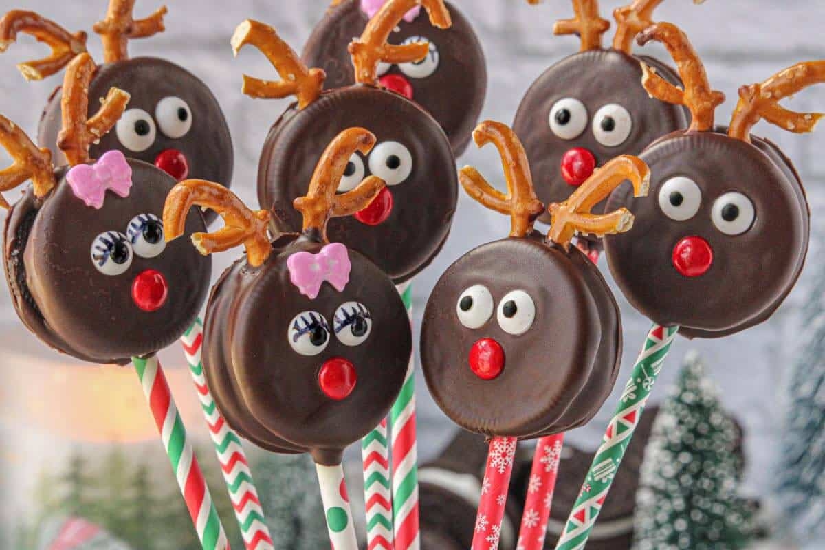 Decorated Reindeer oreo pops displayed upright in front of a snowy holiday scene.