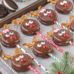 Double Stuf Oreo Reindeer Pops laying out on parchment paper, surrounded by holiday greenery.