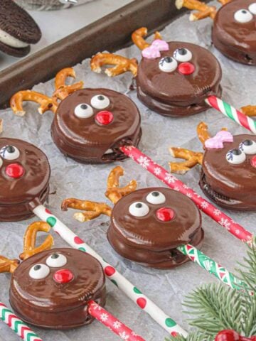 Double Stuf Oreo Reindeer Pops laying out on parchment paper, surrounded by holiday greenery.