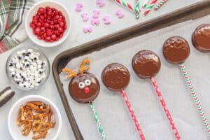 One decorated candy cookie laying on parchment paper with other cookies that have been dipped in chocolate.