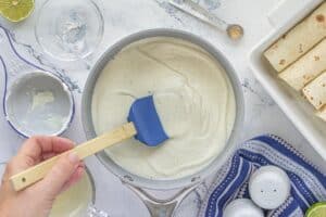 Thick and creamy sour cream enchilada sauce in a saucepan, stirred with a blue spatula.