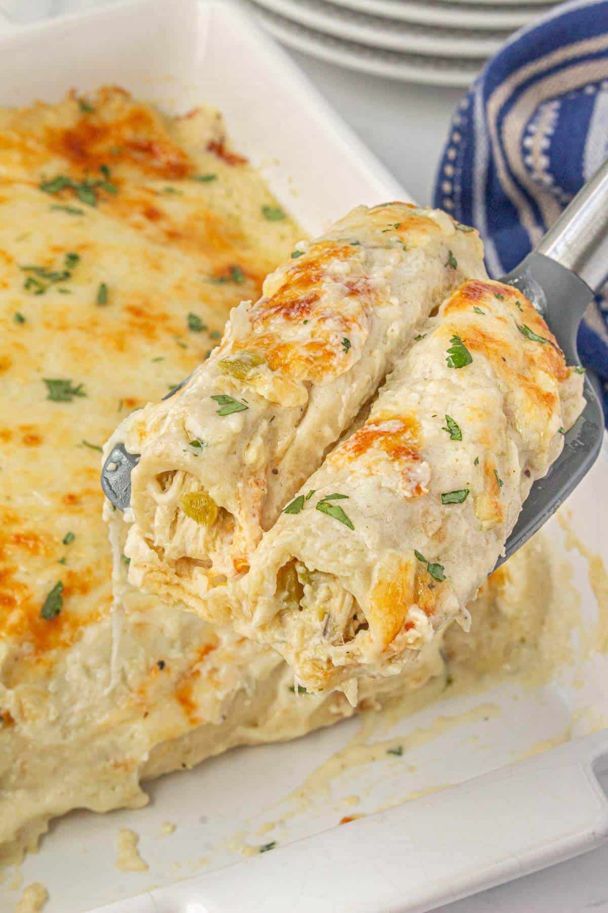 Close-up of two sour cream chicken enchiladas being served from the casserole dish, topped with golden brown cheese and fresh cilantro.