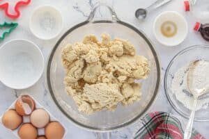Sugar cookie dough in a glass mixing bowl. Flour and eggs are sitting alongside the bowl.