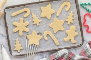 Unbaked cut out cookies being placed on a parchment lined baking sheet with a spatula.