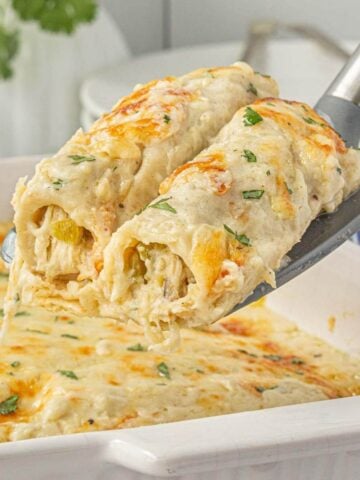 Zoomed-in view of melty, creamy white chicken enchiladas being lifted from the pan—cheese pull and green chiles visible in every bite.