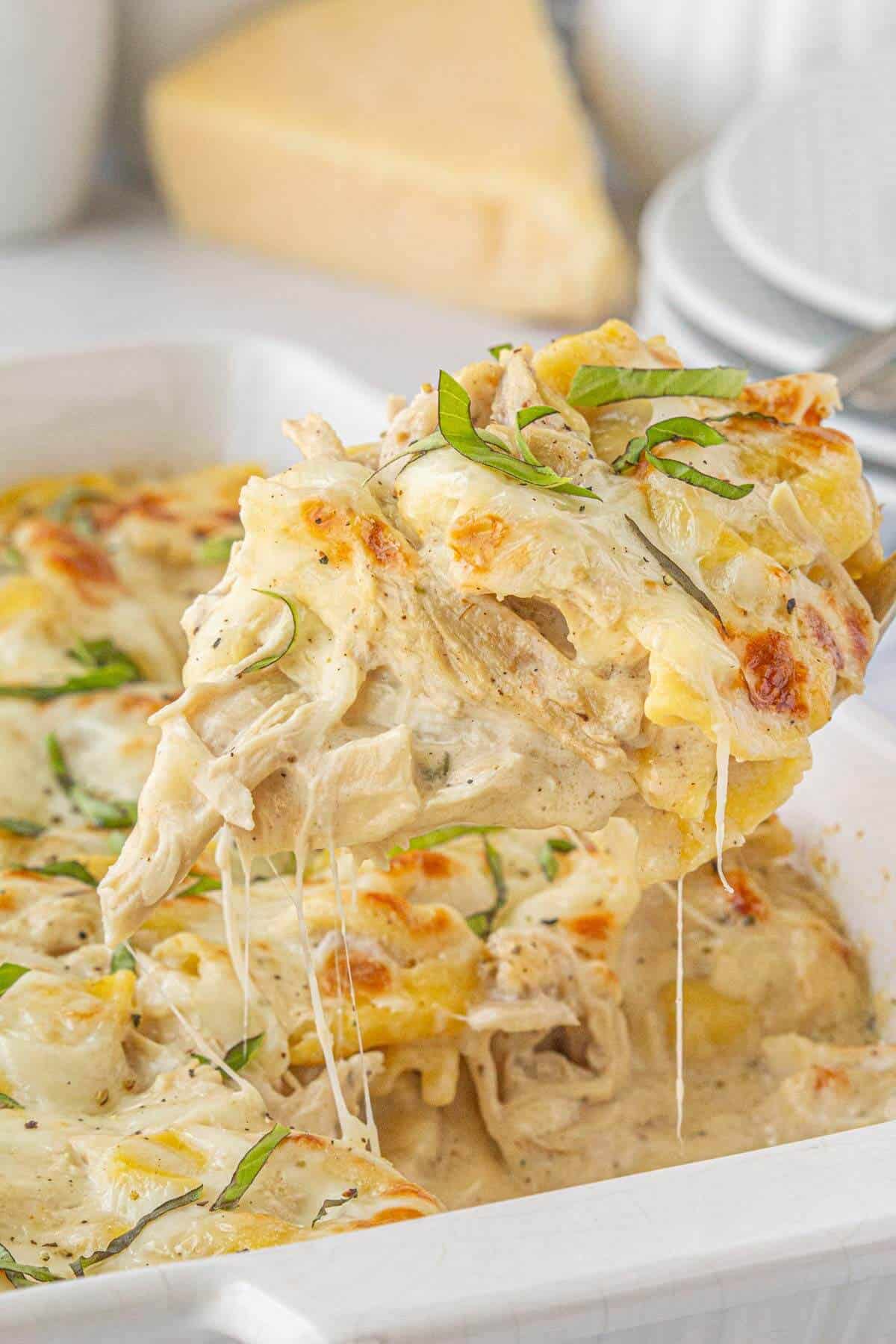 A large cheesy scoop of Chicken Tortellini Bake on a serving spoon, stretching melted cheese from the casserole dish.