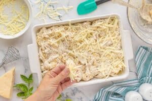 Hand sprinkling shredded cheese over the assembled casserole before baking.