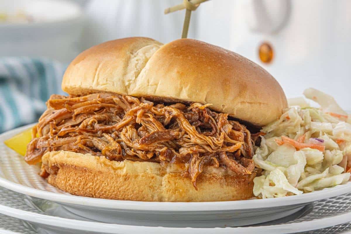 Pulled pork sandwich piled high with saucy shredded pork, served with coleslaw and a pickle spear.