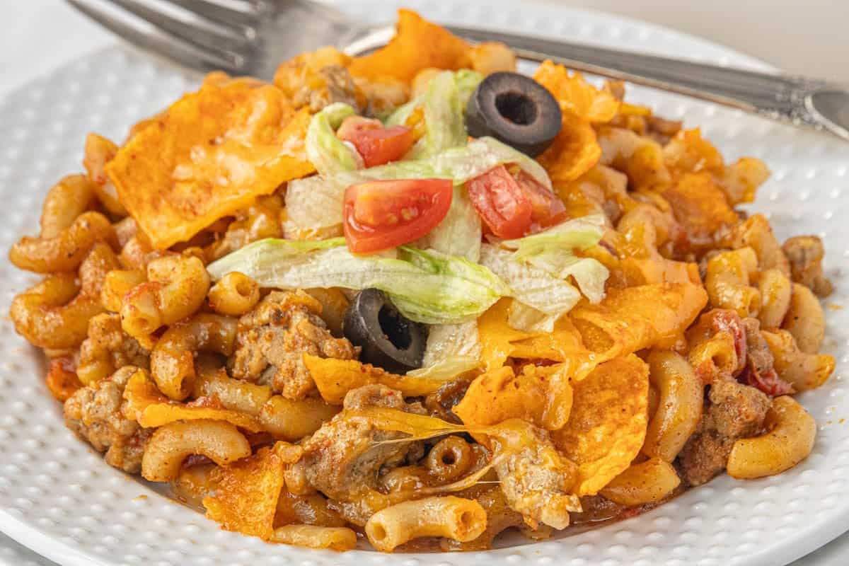 Cheesy Taco Hamburger Helper on a white plate topped with shredded lettuce, tomatoes and olives.