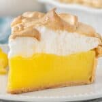 A slice of Lemon Jello Meringue Pie with a golden crust, silky lemon filling, and fluffy toasted meringue topping on a white plate with lemon curls.